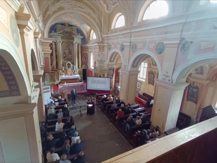 Interno della chiesa dei Santi Ermagora e Fortunato a Gerovo durante la conferenza, con il pubblico e lo schermo delle proiezioni