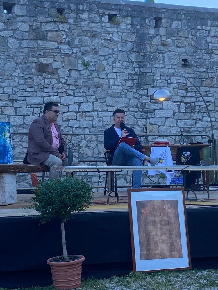 Leone Massimo Occhiuto sul palco di Borgo d'Autore davanti alle mura del Castello di Venosa, con una riproduzione del volto della Sindone in primo piano